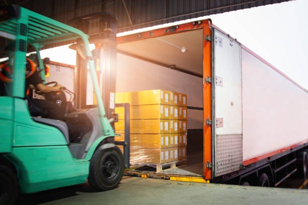 Forklift Driver Loading Package Boxes into Cargo Container. Cargo Trailer Truck Parked Loading at Dock Warehouse. Shipment Delivery Service. Shipping Warehouse Logistics. Freight Truck Transportation.