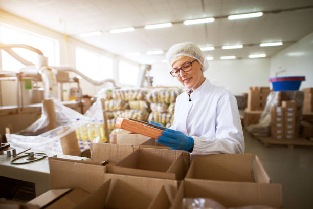 Close up view of a young female pleased worker in sterile cloths packing finished food products in a boxes in food factory storage.