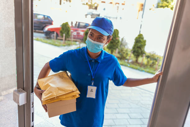 Happy black female courier in face protective medical mask with cardboard box and parcels. She's giving the boxes to the customer.